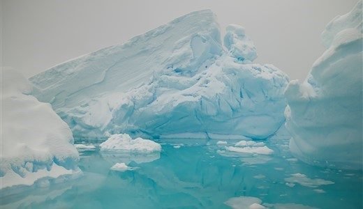 Eisberg in der Antarktis mit wunderschönen Spiegelungen im blauen Wasser.