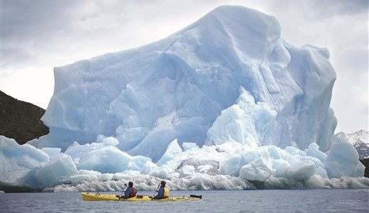 Kanufahrer paddeln vor riesigem Eisberg in Neko Harbour
